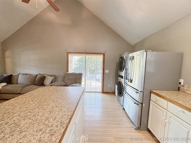 kitchen featuring ceiling fan, light hardwood / wood-style floors, white cabinets, stacked washing maching and dryer, and stainless steel refrigerator