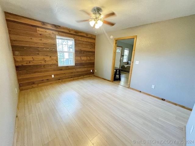 spare room featuring light hardwood / wood-style flooring, wood walls, a textured ceiling, and ceiling fan