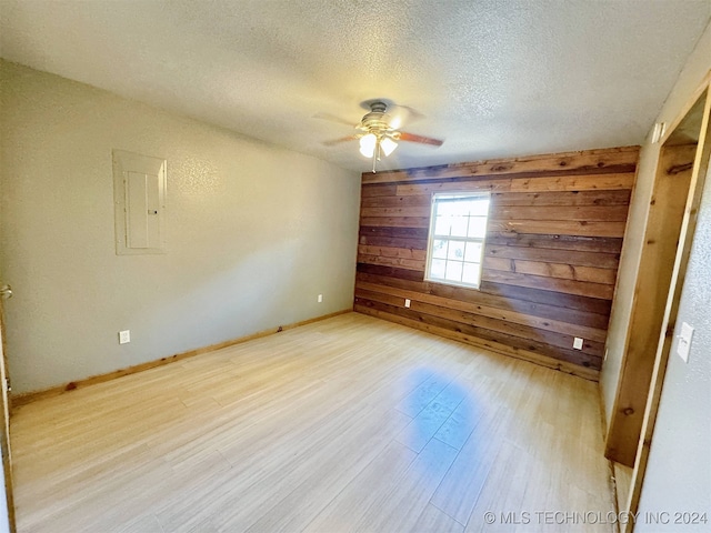 spare room featuring wooden walls, light hardwood / wood-style flooring, electric panel, a textured ceiling, and ceiling fan