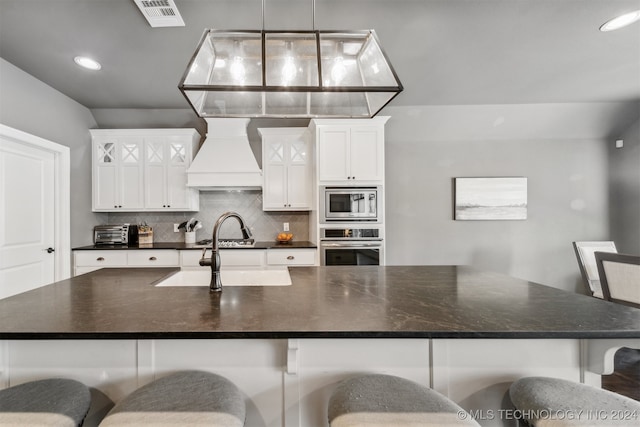 kitchen with premium range hood, appliances with stainless steel finishes, pendant lighting, white cabinetry, and a kitchen breakfast bar