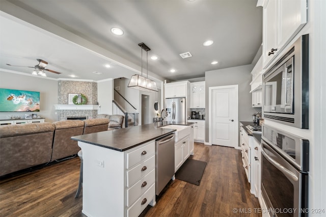 kitchen with white cabinetry, appliances with stainless steel finishes, a fireplace, and an island with sink