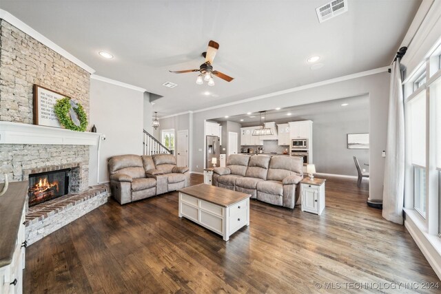 living room with dark hardwood / wood-style flooring, a stone fireplace, crown molding, and ceiling fan