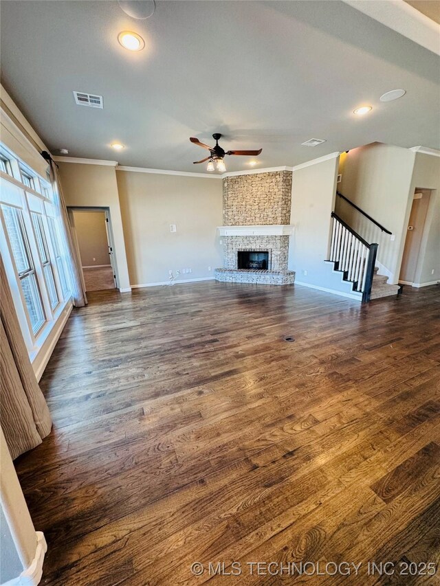 unfurnished living room featuring dark wood-type flooring, ceiling fan, ornamental molding, and a brick fireplace