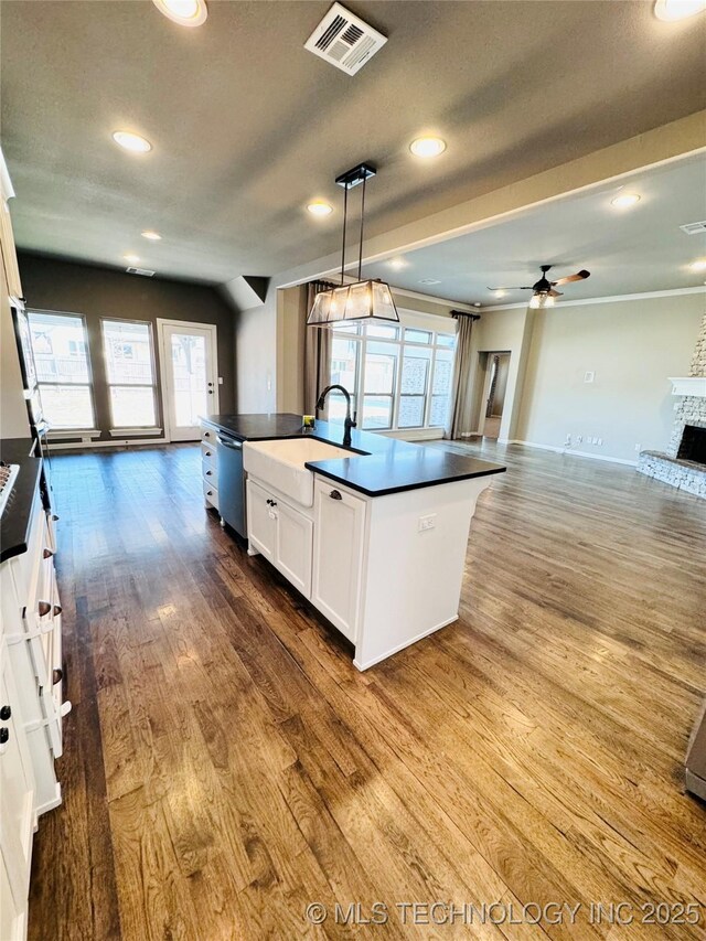 kitchen with wood-type flooring, pendant lighting, a center island with sink, and white cabinets