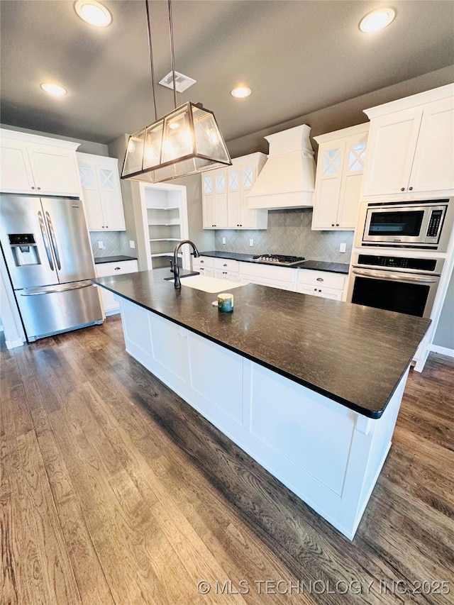 kitchen with custom exhaust hood, decorative light fixtures, a center island with sink, appliances with stainless steel finishes, and white cabinets