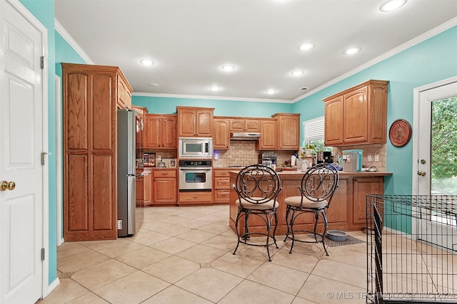 kitchen featuring appliances with stainless steel finishes, kitchen peninsula, light tile patterned flooring, and a kitchen breakfast bar