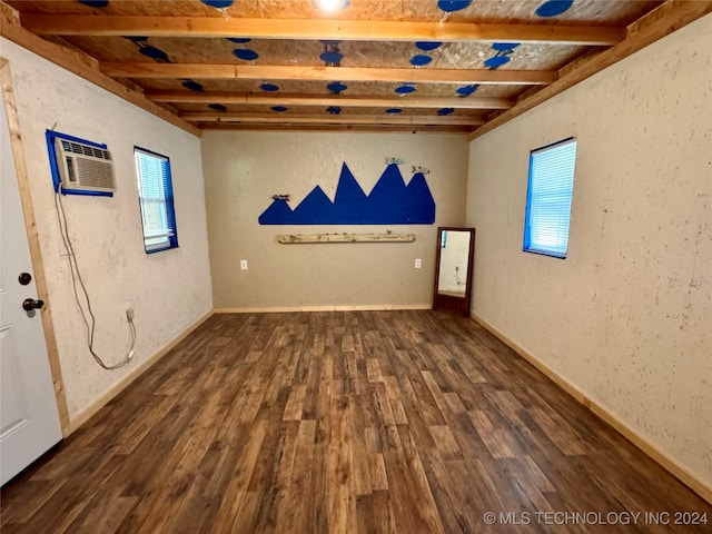 empty room with dark wood-type flooring, a wall unit AC, and beam ceiling