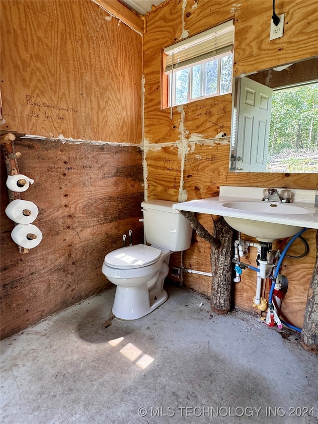 bathroom with toilet, wood walls, and concrete flooring