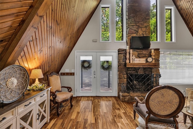 sitting room featuring a stone fireplace, wood ceiling, light hardwood / wood-style flooring, and french doors