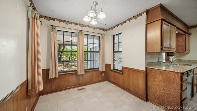 kitchen with wooden walls, light stone countertops, sink, an inviting chandelier, and a textured ceiling