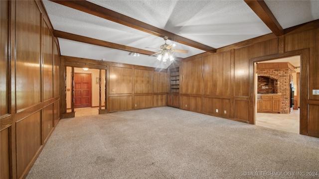 unfurnished room with light colored carpet, beamed ceiling, wooden walls, and a textured ceiling