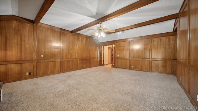 interior space with beamed ceiling, ceiling fan, wood walls, and a textured ceiling