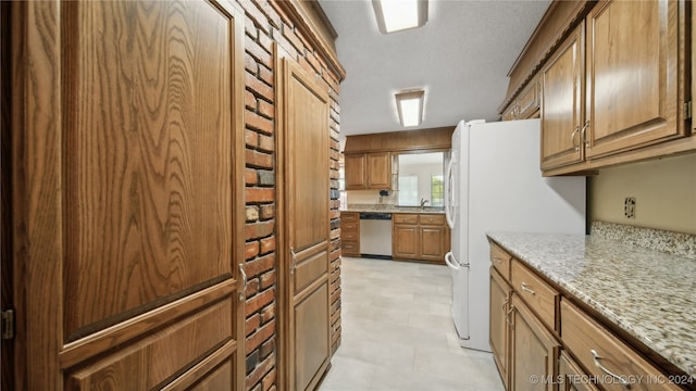 kitchen with a textured ceiling, light stone counters, white refrigerator, and dishwasher