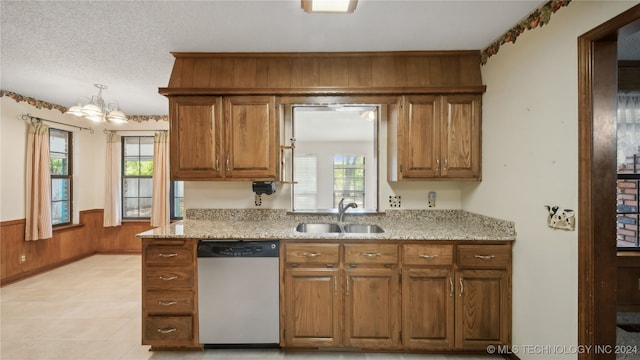 kitchen featuring stainless steel dishwasher, sink, a chandelier, wood walls, and a textured ceiling