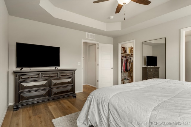 bedroom featuring a tray ceiling, a closet, hardwood / wood-style floors, a spacious closet, and ceiling fan