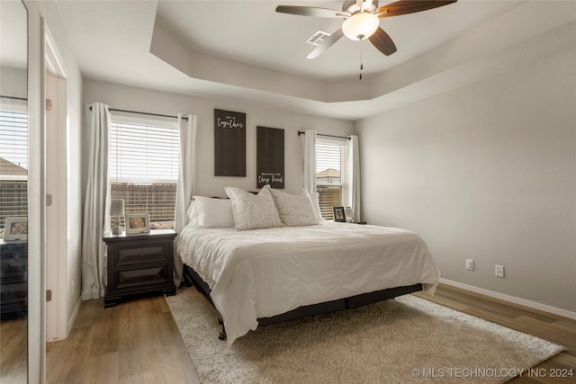 bedroom with ceiling fan, a tray ceiling, and light hardwood / wood-style floors