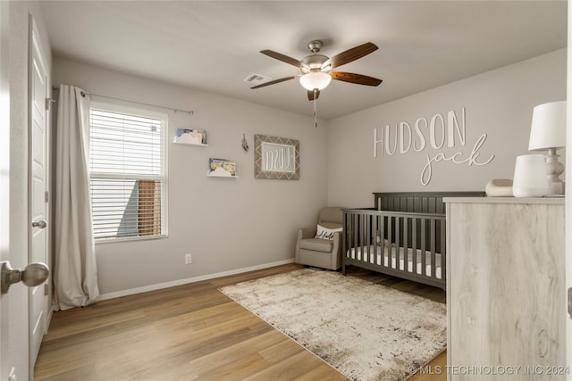 bedroom featuring ceiling fan, a crib, and hardwood / wood-style floors