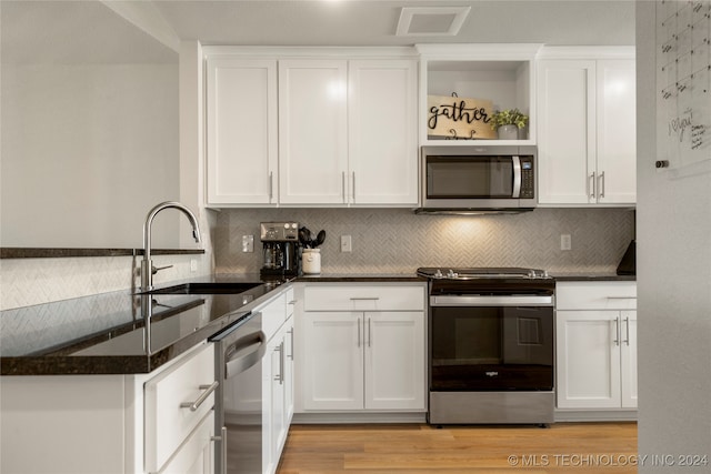 kitchen with dark stone countertops, light hardwood / wood-style flooring, appliances with stainless steel finishes, and white cabinetry