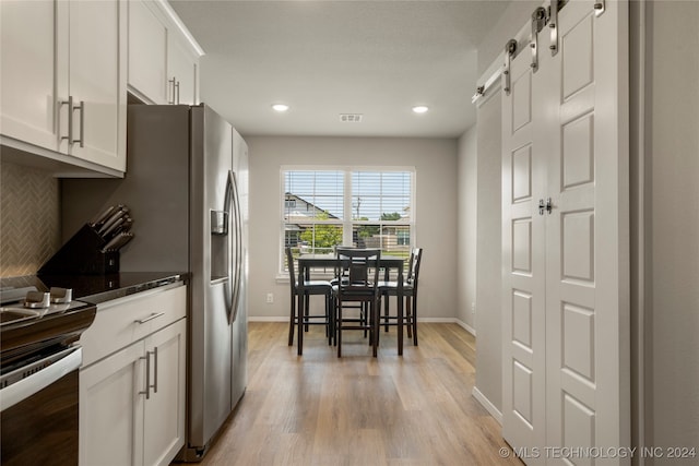 kitchen with white cabinets, light hardwood / wood-style floors, stainless steel range, and tasteful backsplash