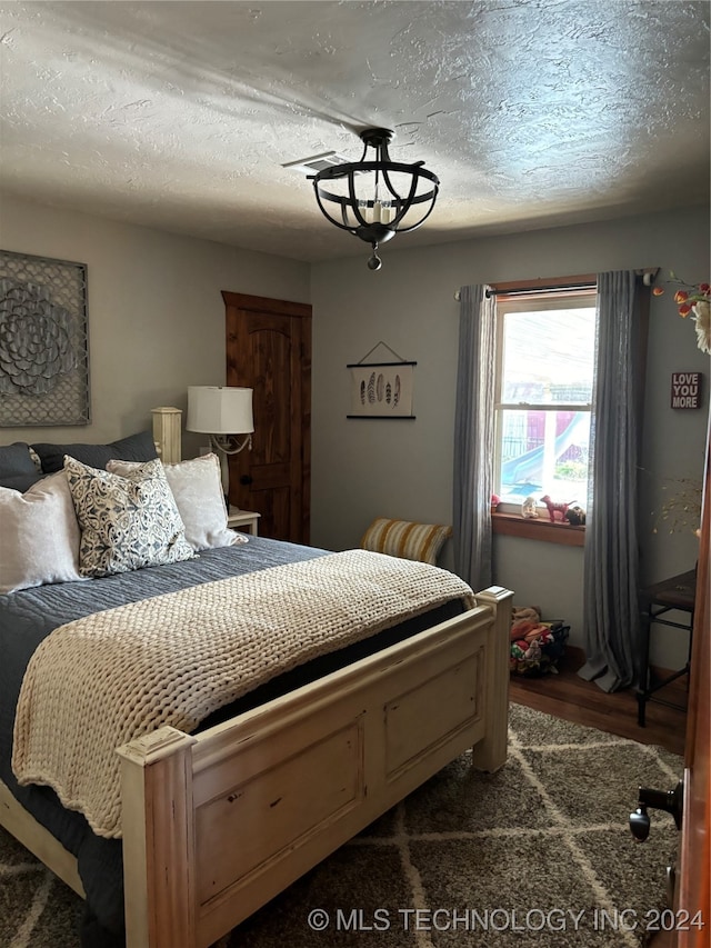 bedroom featuring dark wood-type flooring, a textured ceiling, and an inviting chandelier