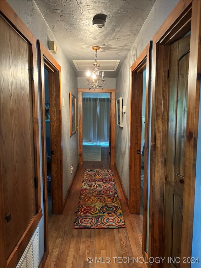 corridor featuring a textured ceiling, wood-type flooring, and an inviting chandelier