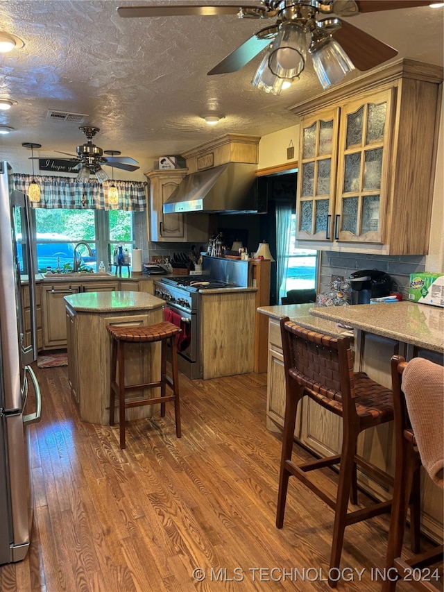 kitchen featuring wall chimney range hood, a kitchen breakfast bar, wood-type flooring, stainless steel appliances, and a center island