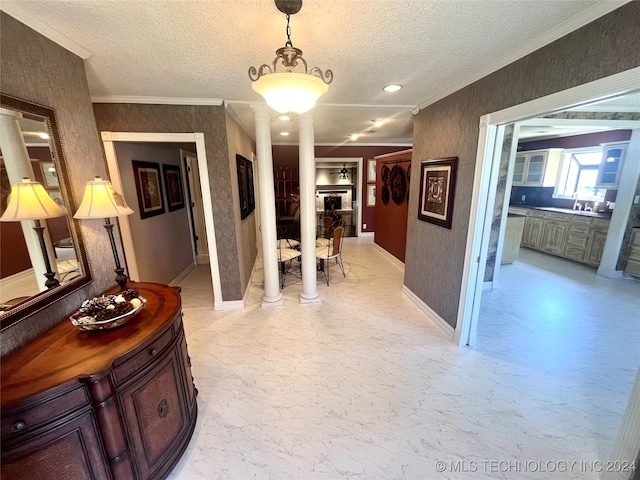 hall with a textured ceiling, crown molding, and ornate columns