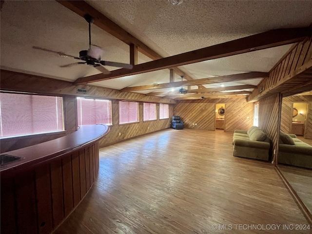 unfurnished living room with a textured ceiling, hardwood / wood-style flooring, ceiling fan, and wooden walls