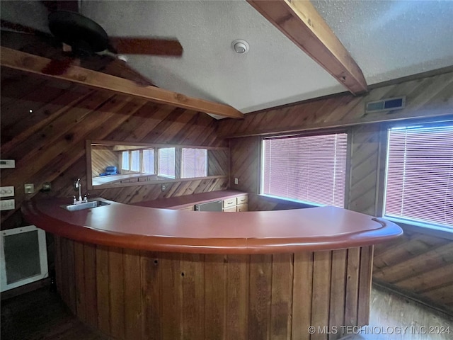 bar with a textured ceiling, wood walls, sink, and lofted ceiling with beams