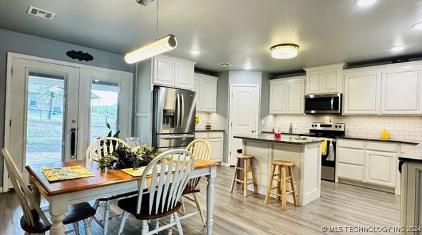 kitchen with appliances with stainless steel finishes, white cabinetry, light wood-type flooring, french doors, and decorative light fixtures