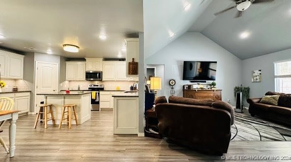 living room featuring sink, ceiling fan, lofted ceiling, and light wood-type flooring