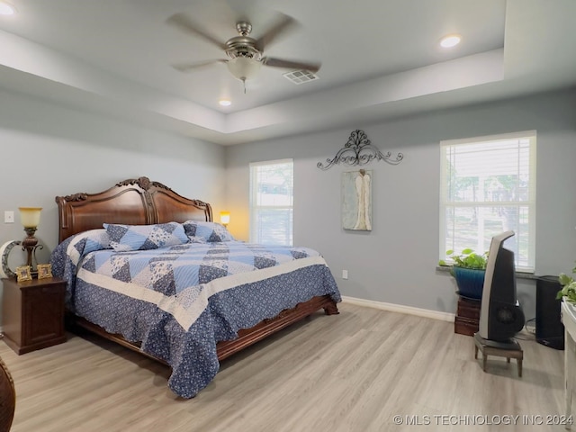 bedroom with light hardwood / wood-style floors, a raised ceiling, and ceiling fan