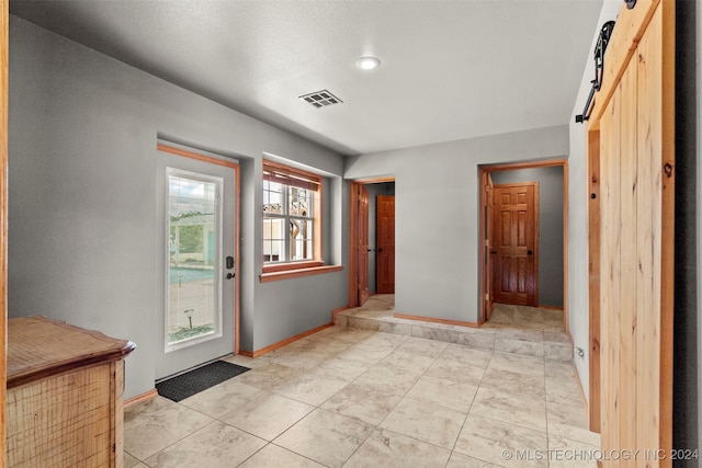 doorway with a barn door, light tile patterned floors, and a healthy amount of sunlight