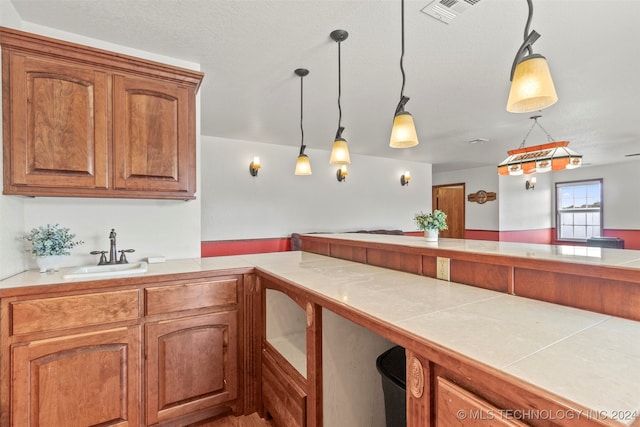 kitchen with tile countertops, hanging light fixtures, kitchen peninsula, and sink