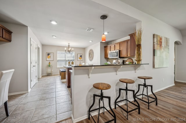 kitchen with kitchen peninsula, a breakfast bar, a chandelier, light hardwood / wood-style floors, and hanging light fixtures