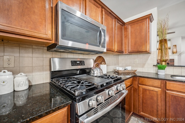 kitchen featuring sink, backsplash, appliances with stainless steel finishes, and dark stone counters