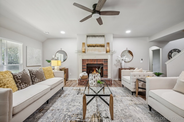 living room featuring ceiling fan, hardwood / wood-style floors, vaulted ceiling, and a brick fireplace