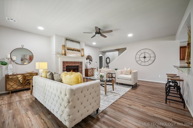 living room featuring ceiling fan, hardwood / wood-style floors, and a brick fireplace