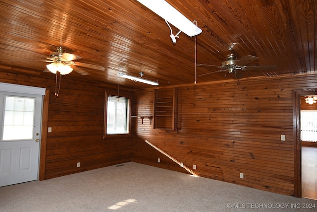 carpeted spare room featuring ceiling fan, wood walls, and wood ceiling