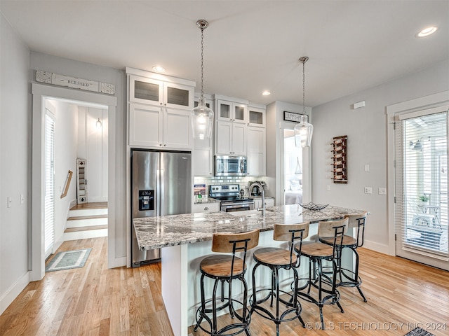 kitchen with white cabinets, light stone counters, stainless steel appliances, light hardwood / wood-style floors, and a center island with sink