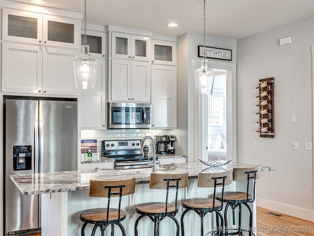 kitchen featuring appliances with stainless steel finishes, light stone countertops, light hardwood / wood-style floors, white cabinetry, and a kitchen island with sink