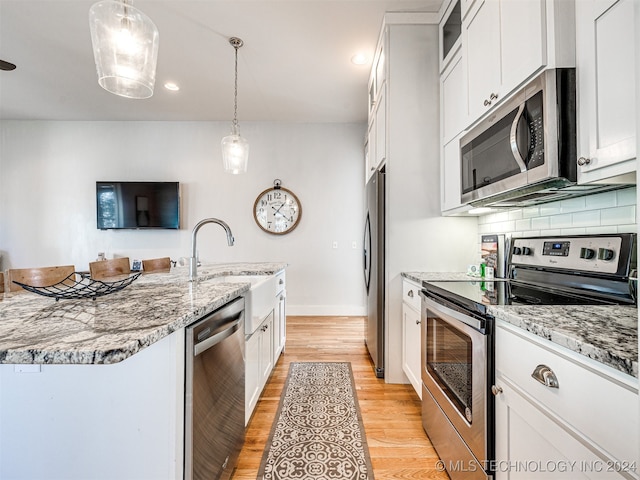 kitchen featuring light wood-type flooring, pendant lighting, backsplash, appliances with stainless steel finishes, and a center island with sink