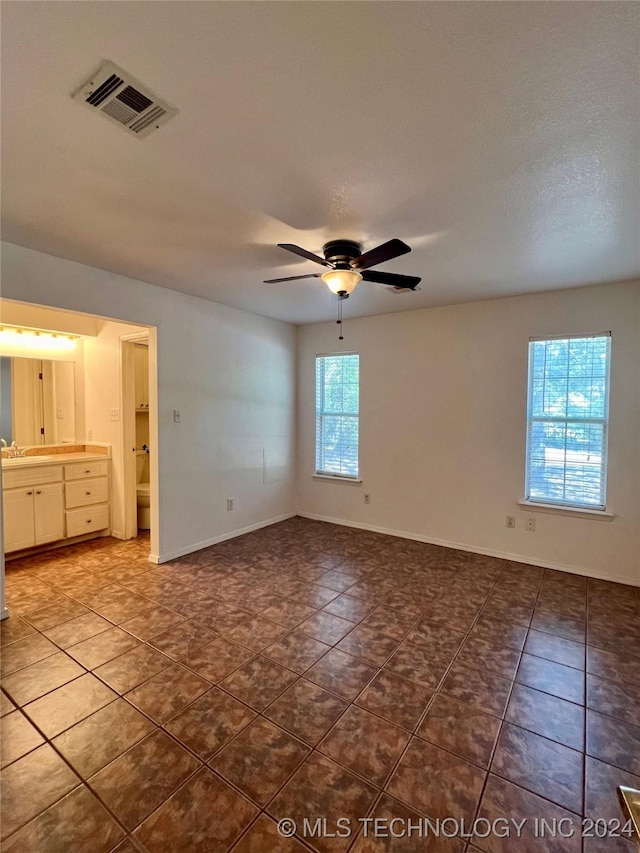 unfurnished bedroom featuring connected bathroom, dark tile patterned flooring, and ceiling fan