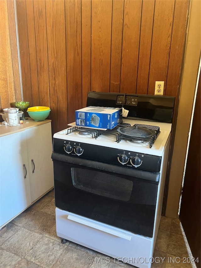 kitchen featuring white stove, wooden walls, and tile patterned flooring