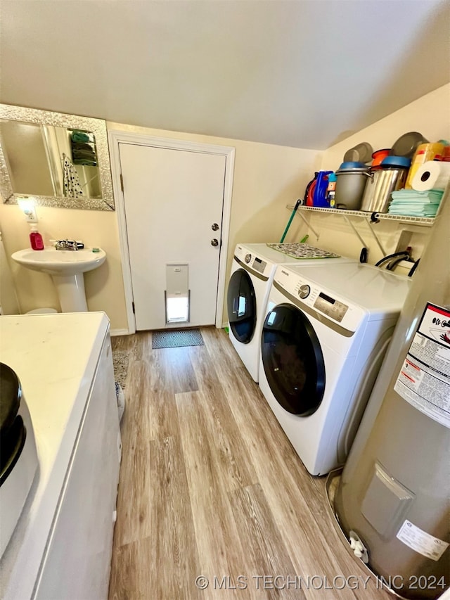 laundry area with light hardwood / wood-style floors, electric water heater, washer and dryer, and sink