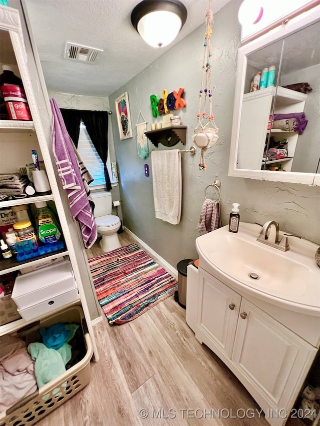 bathroom with hardwood / wood-style floors, a textured ceiling, vanity, and toilet