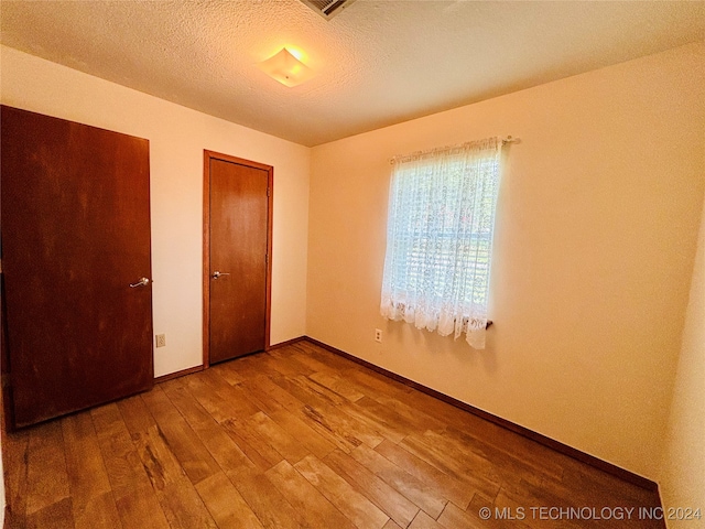 unfurnished room with a textured ceiling and wood-type flooring