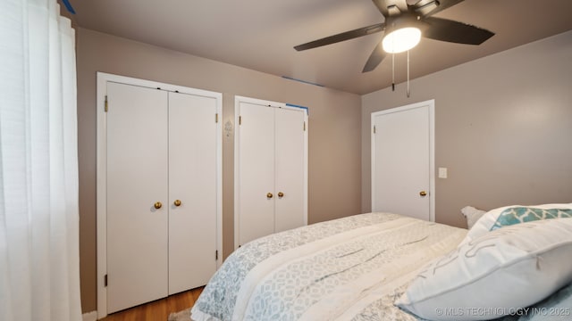 bedroom with ceiling fan, wood-type flooring, and multiple closets