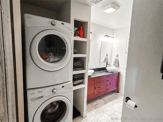 laundry area featuring light tile patterned floors, a textured ceiling, and stacked washer / drying machine