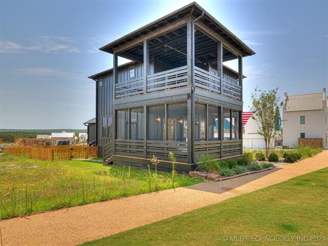 view of front of property featuring board and batten siding, fence, a balcony, and a front lawn